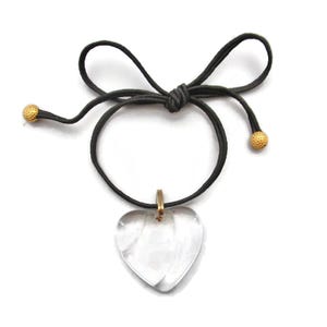 May include: A clear heart-shaped pendant necklace with a gold-toned chain and black cord. The cord has gold-toned beads at each end.