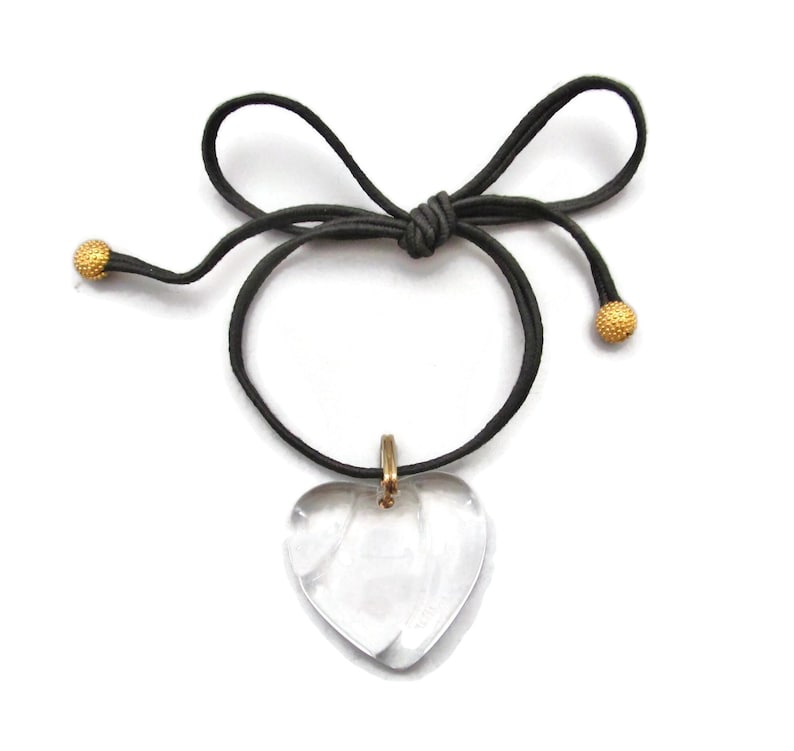 May include: A clear heart-shaped pendant necklace with a gold-toned chain and black cord. The cord has gold-toned beads at each end.