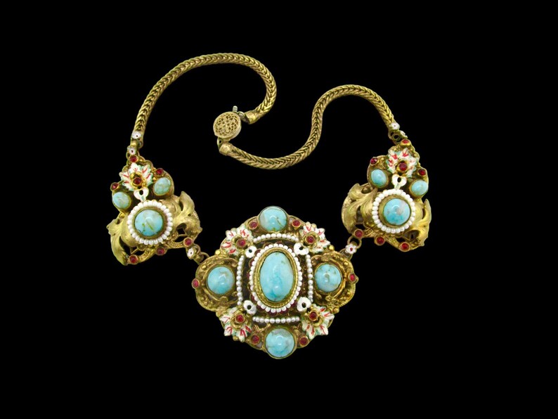 Peut inclure: Un collier en or avec un grand pendentif turquoise central et de plus petites pierres turquoise. Le collier est d&eacute;cor&eacute; d'&eacute;mail rouge et blanc et de petites perles.
