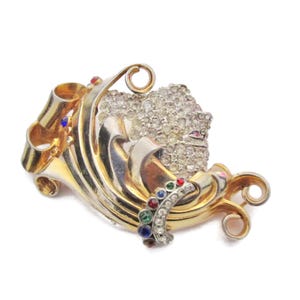 May include: A gold and silver tone brooch with a swirl design and a cluster of clear rhinestones. The brooch is accented with red, blue, and green gemstones.