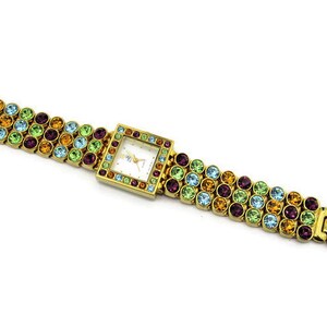 May include: A gold-tone watch with a square face and a multi-colored crystal-encrusted band. The band features rows of green, blue, orange, and purple crystals.