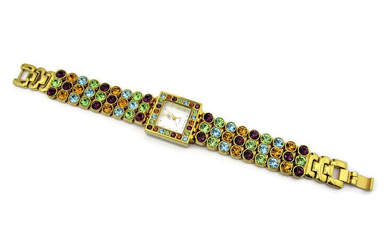 May include: A gold-tone watch with a square face and a multi-colored crystal-encrusted band. The band features rows of green, blue, orange, and purple crystals.
