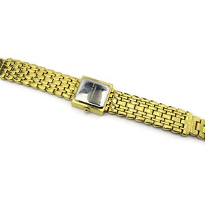 May include: A gold-tone watch with a square face and a gold metal band. The watch has a silver face with black markings.