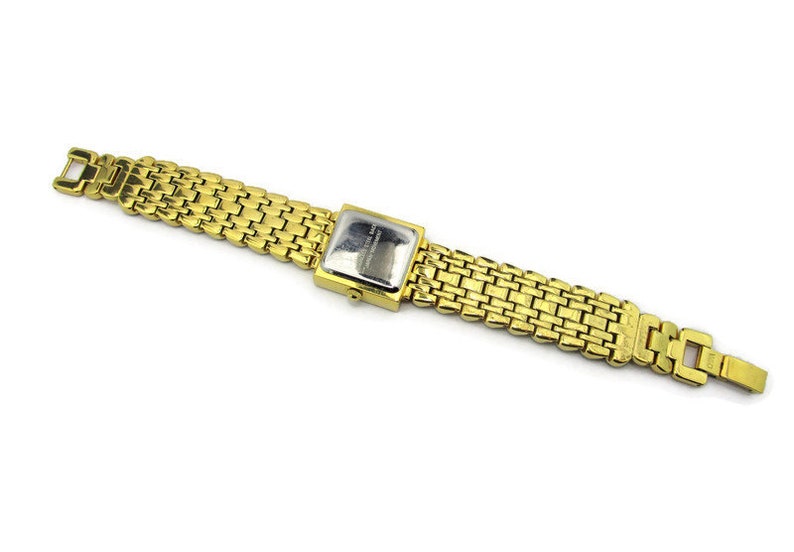 May include: A gold-tone watch with a square face and a gold metal band. The watch has a silver face with black markings.