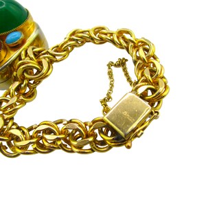 May include: A gold chain bracelet with a large green, blue, and red gemstone pendant. The bracelet has a lobster claw clasp.