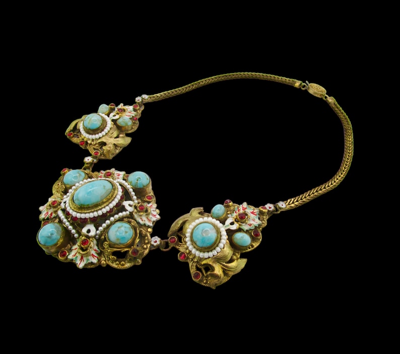 Peut inclure: Un collier en or avec des pierres turquoise et rouges. Le collier a une cha&icirc;ne et trois pendentifs aux motifs complexes.