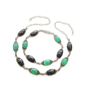 Puede incluir: Un collar de cadena de plata con piedras ovaladas negras y verdes alternas. El collar est&aacute; hecho de una cadena delicada con peque&ntilde;os detalles brillantes.