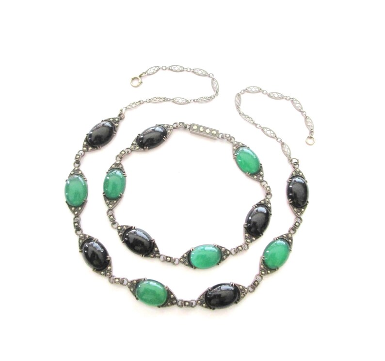 Puede incluir: Un collar de cadena de plata con piedras ovaladas negras y verdes alternas. El collar est&aacute; hecho de una cadena delicada con peque&ntilde;os detalles brillantes.