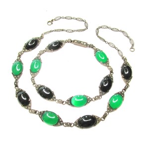 Puede incluir: Un collar de cadena de plata con piedras ovaladas negras y verdes alternas. Las piedras est&aacute;n engastadas en plata con un dise&ntilde;o delicado. La cadena est&aacute; hecha de peque&ntilde;os c&iacute;rculos unidos.