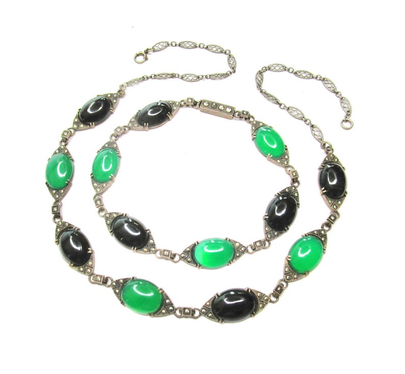 Puede incluir: Un collar de cadena de plata con piedras ovaladas negras y verdes alternas. Las piedras est&aacute;n engastadas en plata con un dise&ntilde;o delicado. La cadena est&aacute; hecha de peque&ntilde;os c&iacute;rculos unidos.