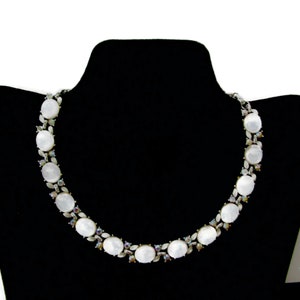 Puede incluir: Un collar blanco y plateado con piedras blancas de forma ovalada y piedras iridiscentes más pequeñas.