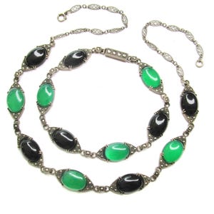 Puede incluir: Un collar de cadena de plata con piedras ovaladas negras y verdes alternas. Las piedras est&aacute;n engastadas en plata con un dise&ntilde;o de marcasita. El collar es de doble cadena y tiene una cadena delicada.