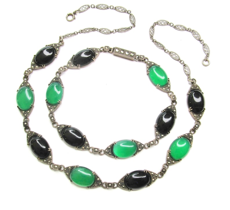 Puede incluir: Un collar de cadena de plata con piedras ovaladas negras y verdes alternas. Las piedras est&aacute;n engastadas en plata con un dise&ntilde;o de marcasita. El collar es de doble cadena y tiene una cadena delicada.