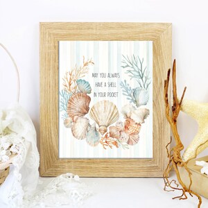 May include: A framed print with a watercolor illustration of seashells and coral. The text reads, "May you always have a shell in your pocket." The frame is light brown, and the background is a light blue and white striped pattern.