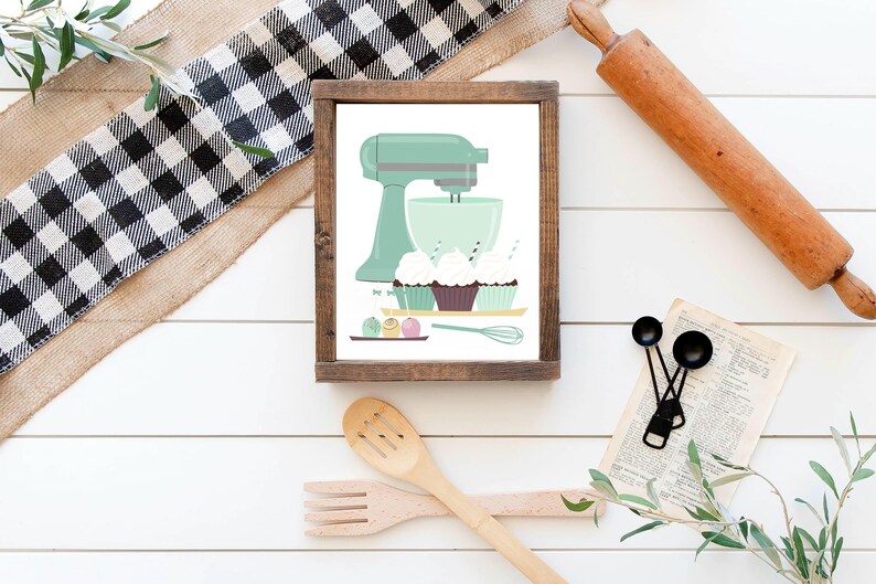 May include: A framed illustration of a green stand mixer with a bowl and cupcakes. The cupcakes are decorated with sprinkles and frosting. There are also some colorful sprinkles on the table.