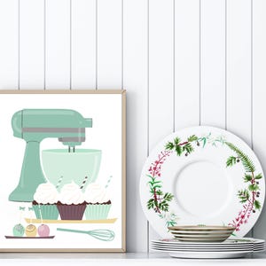 May include: A framed illustration of a green stand mixer with a bowl and three cupcakes with green, brown, and white frosting. The cupcakes are on a tray with a whisk and three round candies.