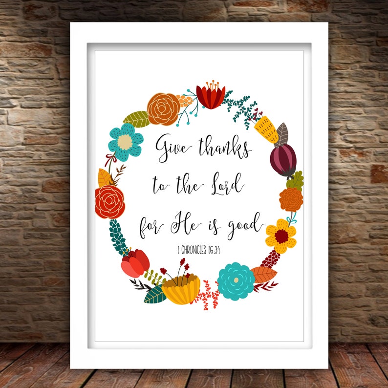 May include: A white framed print with a floral wreath design. The wreath is made up of colorful flowers in shades of red, orange, yellow, blue, and green. The text inside the wreath reads "Give thanks to the Lord for He is good. 1 Chronicles 16:34".