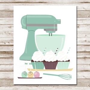 May include: A mint green stand mixer with a white bowl and a whisk attachment. Three cupcakes with white frosting and sprinkles are on a tray in front of the mixer. Three cake pops are on a tray below the cupcakes.