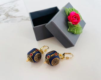 May include: A pair of gold earrings with blue and red round beads. The earrings are in a small gray box with a pink flower.