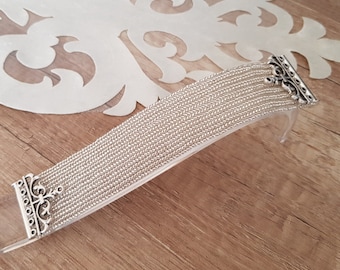 May include: A silver bracelet with a delicate chain design and ornate clasps. The bracelet is made of multiple strands of chain, creating a layered effect.