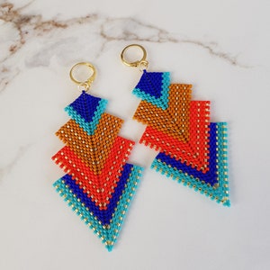 May include: A pair of geometric dangle earrings with a layered design. The earrings are made with blue, orange, and turquoise beads and have gold-toned hooks.