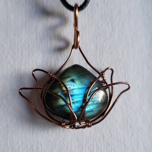 May include: A copper wire wrapped pendant featuring a blue and green labradorite gemstone. The pendant is suspended from a black cord.