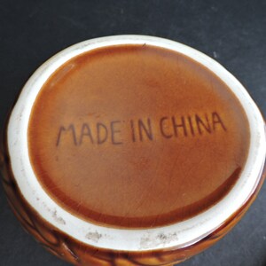 May include: A brown ceramic bowl with a textured exterior and a white rim. The words "MADE IN CHINA" are printed in brown on the interior base of the bowl. The bowl is likely vintage.