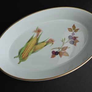 May include: White oval serving platter with a gold rim. The platter features a colorful illustration of two ears of corn and a sprig of blackberries. The design is centered on the platter, which is set against a black background.