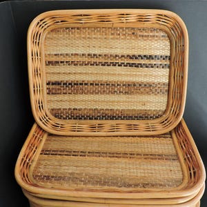 May include: Stack of rectangular woven rattan trays. The trays have a light brown border and a woven pattern in shades of brown, beige, and black. The trays are designed for serving or display.