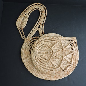 Könnte beinhalten: Gewebter schwanförmiger Korb aus Stroh mit rundem Körper und langem, gebogenem Hals, der einen Griff bildet. Der Korb hat ein Sternmuster auf der Vorderseite und besteht aus naturfarbenem Stroh.