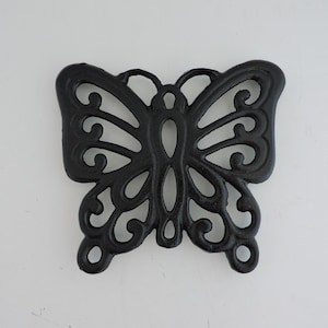 Puede incluir: Salvamanteles negro de hierro fundido con forma de mariposa. El salvamanteles presenta un diseño calado con intrincados patrones de remolinos. Las alas y el cuerpo de la mariposa están claramente definidos, creando un accesorio de cocina decorativo y funcional.