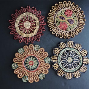 Puede incluir: Cuatro posavasos redondos decorativos con intrincados diseños tejidos. Cada posavasos presenta una combinación de colores única, incluyendo rojo, verde, azul y dorado, con patrones florales y geométricos. Estos posavasos son ideales para proteger superficies.