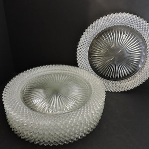 Puede incluir: Un conjunto de platos de vidrio transparente con un borde texturizado con diseño de diamantes y un diseño central en forma de estrella. Varios platos están apilados, con uno separado. Los platos están sobre una superficie oscura.
