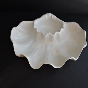 May include: White, scalloped-edge serving dish with a three-section design. The dish has a glossy finish and a textured, petal-like pattern. The dish is made of ceramic or porcelain.