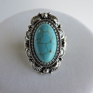 May include: A silver-toned ring featuring an oval, turquoise-colored stone with a webbed pattern. The stone is set within a decorative, filigree-style frame. The ring has a vintage or Southwestern aesthetic.