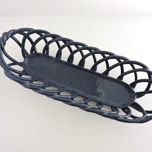 May include: A dark blue, oval-shaped basket with a matching, smaller tray inside. The basket has a woven design with a glossy finish, and the tray is smooth. The basket is empty and sits on a white surface.