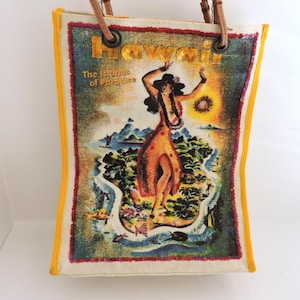 May include: A rectangular tote bag with yellow fabric trim and brown leather handles. The front features a colorful graphic of a hula dancer on an island with the text Hawaii and The Islands of Paradise in gold lettering at the top.