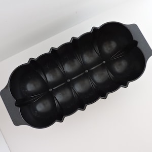 May include: A black rectangular baking mold with a scalloped edge design featuring eight individual rounded compartments arranged in two rows. The mold includes two integrated handles on opposite ends and a smooth, matte finish throughout.