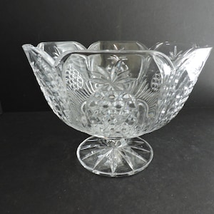 Könnte beinhalten: Eine transparente Kristallschale mit einem gewellten Rand. Die Schale weist ein Diamantenmuster und Traubenmuster auf. Sie steht auf einem runden, sternförmigen Sockel, ideal zum Servieren von Obst oder zur Präsentation von Dekorationsartikeln.