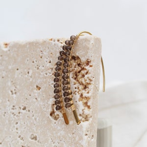 May include: Gold wire earrings with brown gemstone beads. The earrings are dangling and have a curved shape.