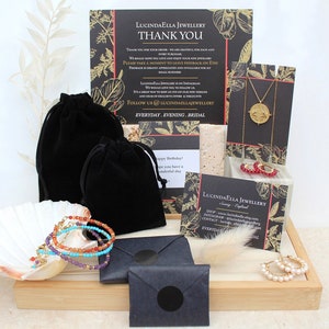 May include: A collection of jewelry items, including necklaces, bracelets, and earrings, displayed on a wooden tray. The jewelry is packaged in black velvet bags and envelopes. The image also includes a thank you card from the shop, Lucindaella Jewellery.