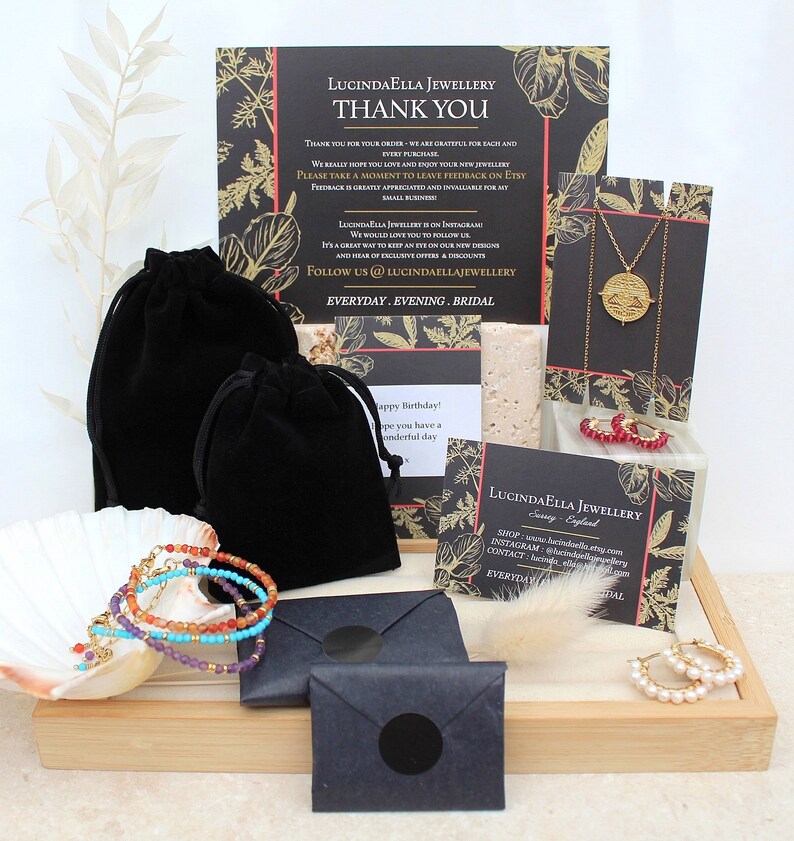 May include: A collection of jewelry items, including necklaces, bracelets, and earrings, displayed on a wooden tray. The jewelry is packaged in black velvet bags and envelopes. The image also includes a thank you card from the shop, Lucindaella Jewellery.