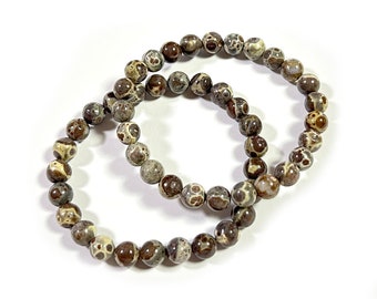Può includere: Due braccialetti di perline marroni e bianche con motivo. I braccialetti sono fatti di perline rotonde con un motivo maculato.