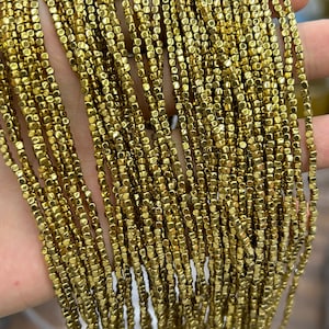 May include: A strand of gold-toned square beads. The beads are small and have a metallic finish.