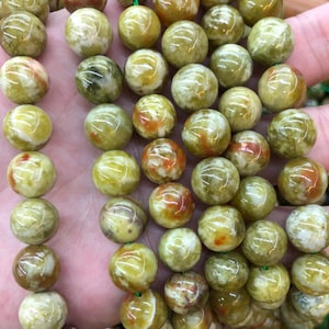 Pode incluir: Um fio de contas redondas verdes, brancas e marrons. As contas são feitas de um material translúcido com um padrão manchado.