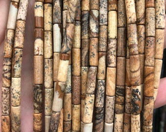 May include: A strand of brown, beige, and white patterned cylindrical gemstone beads. The beads are approximately 1 cm in diameter and 2 cm in length.