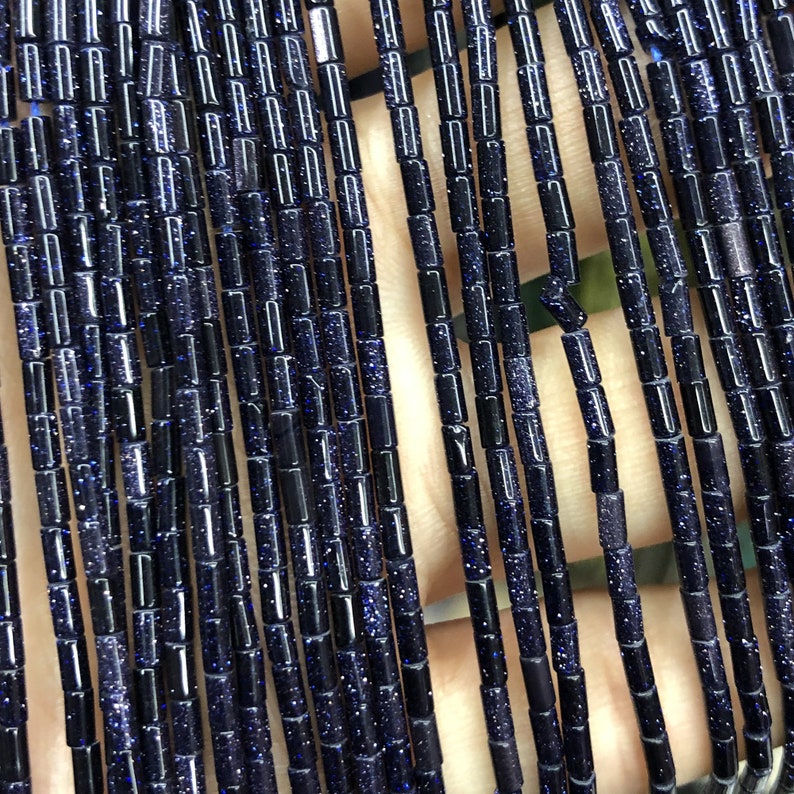 Op de afbeelding: Een streng donkerblauwe, glinsterende, gefacetteerde, buisvormige kralen. De kralen zijn ongeveer 10 mm lang en 4 mm breed.