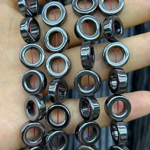 May include: A strand of black hematite beads with a hole in the center of each bead. The beads are smooth and shiny.