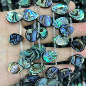 May include: A strand of iridescent abalone shell beads in a teardrop shape. The beads are strung on clear elastic cord and have a variety of colors, including green, blue, and purple.