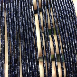Op de afbeelding: Een streng donkerblauwe edelsteen kralen, elke kraal is een kleine cilinder met een gespikkelde textuur.